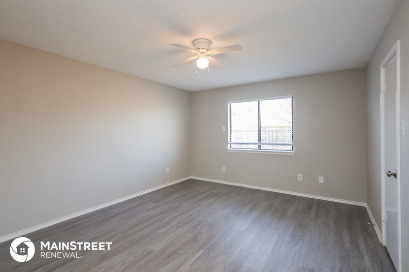 the spacious living room with wood flooring and a ceiling fan