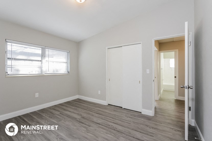 the living room of an apartment with white walls and wood flooring