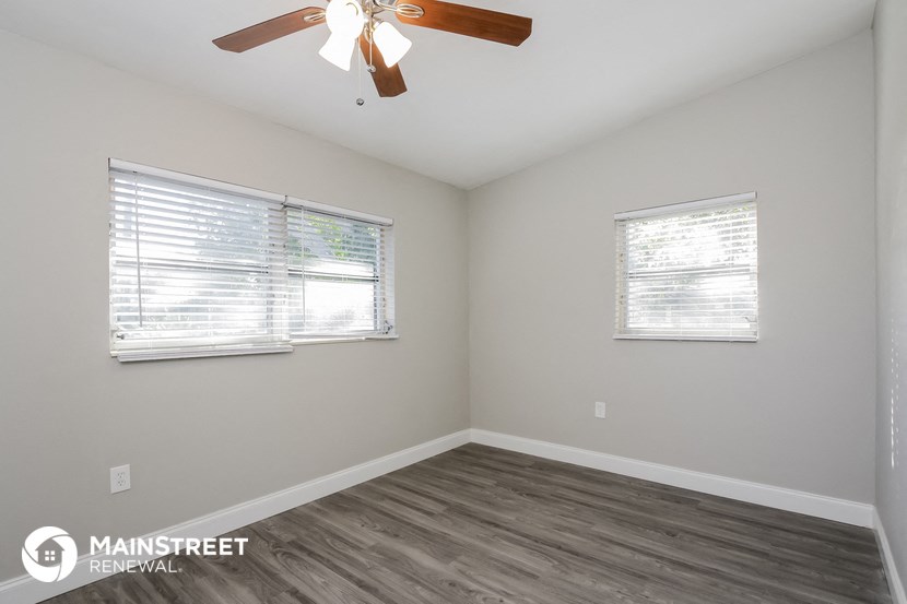 the living room of an apartment with a ceiling fan and two windows