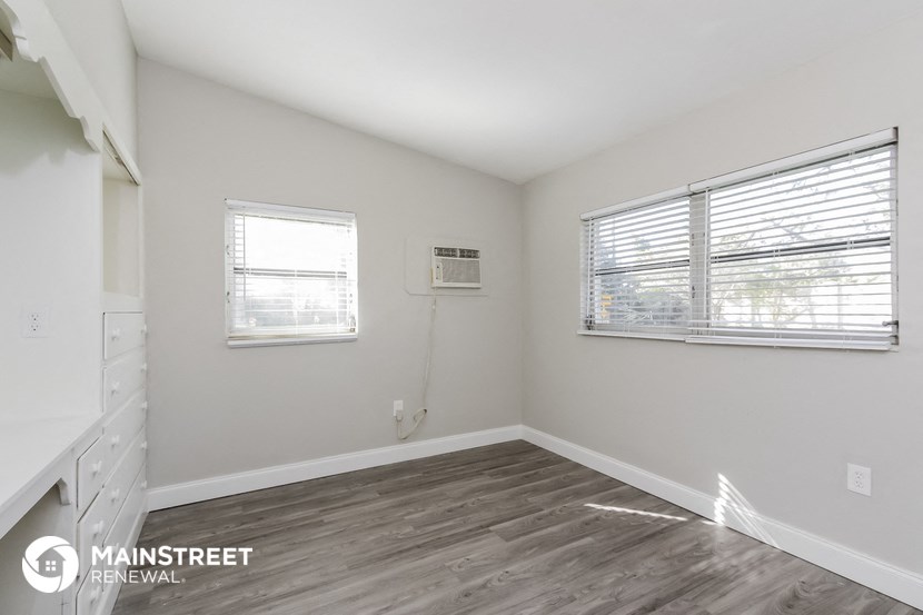 the living room of an apartment with white walls and wood flooring
