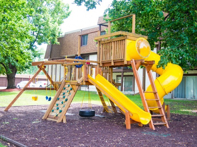 a playground with a yellow slide and playset in a backyard