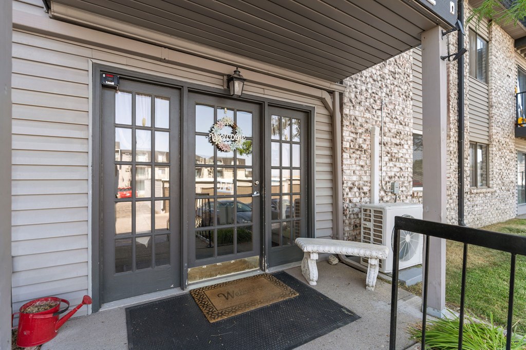 A grey door with a glass window and a mat in front of it.
