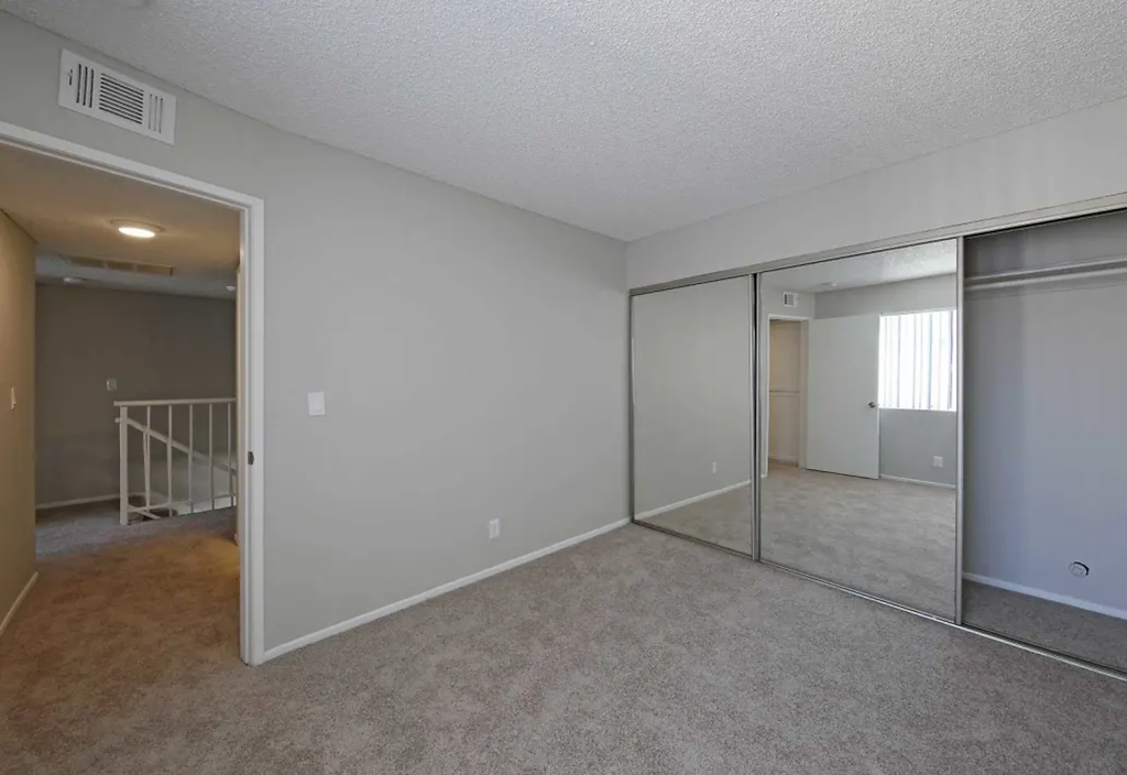 an empty living room with a mirrored closet and a staircase