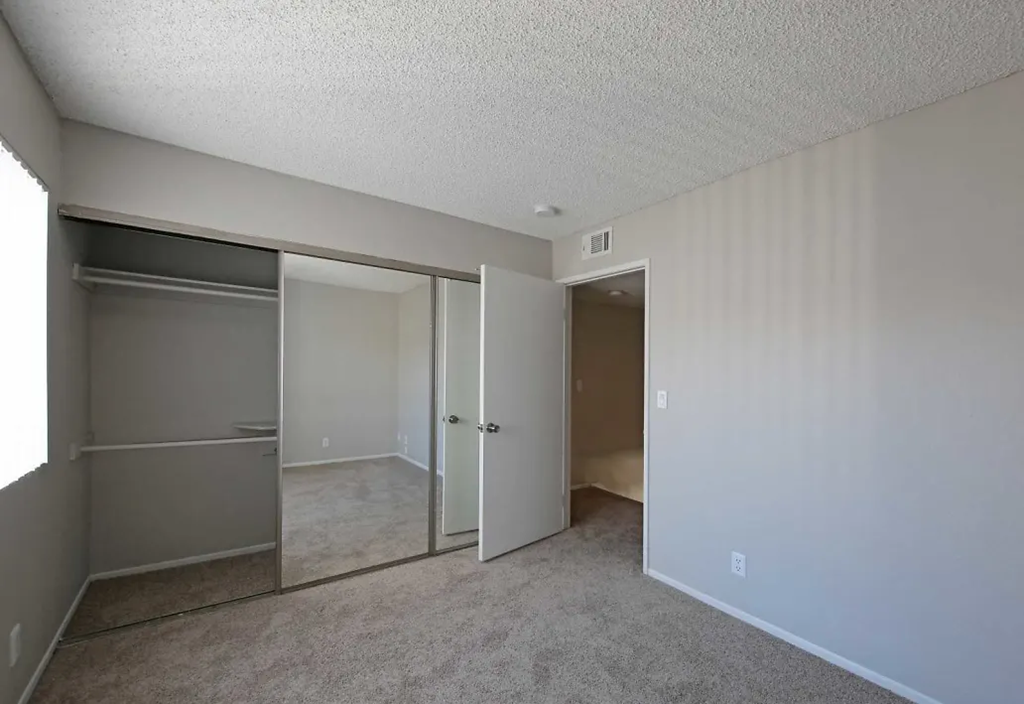 an empty bedroom with a closet and a mirrored door