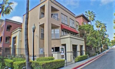 A street view of a beige building with a red awning and a palm tree in front.