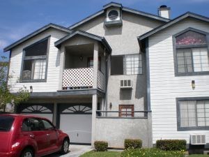 A red car is parked in front of a two-story house.