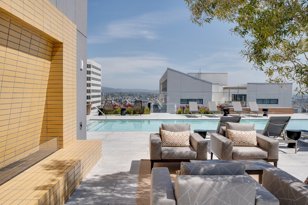 a swimming pool with chairs and couches on a roof top overlooking a city