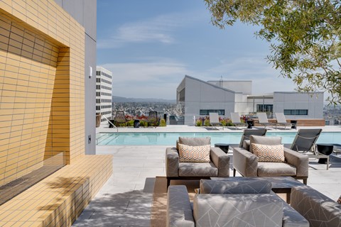 a swimming pool with chairs and couches on a roof top overlooking a city