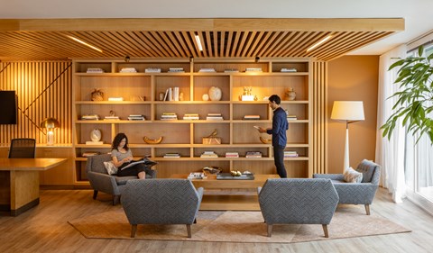 a man and a woman sitting in a living room in front of a wooden shelf