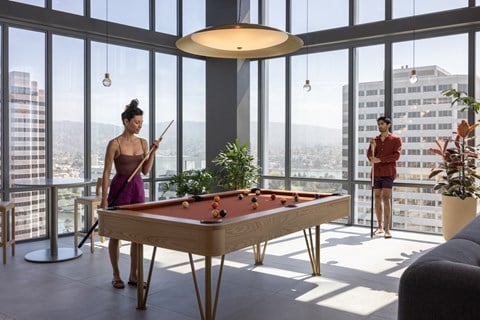 a woman standing next to a pool table in a living room with windows