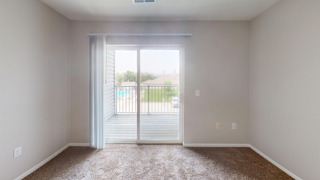A room with a carpeted floor and a sliding glass door leading to a deck.
