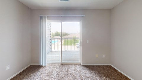 A room with a carpeted floor and a sliding glass door leading to a deck.