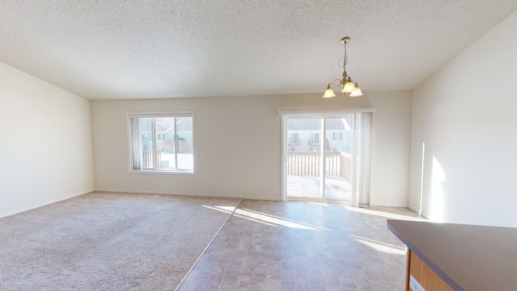 the living room and dining room of an empty house with a door to a balcony
