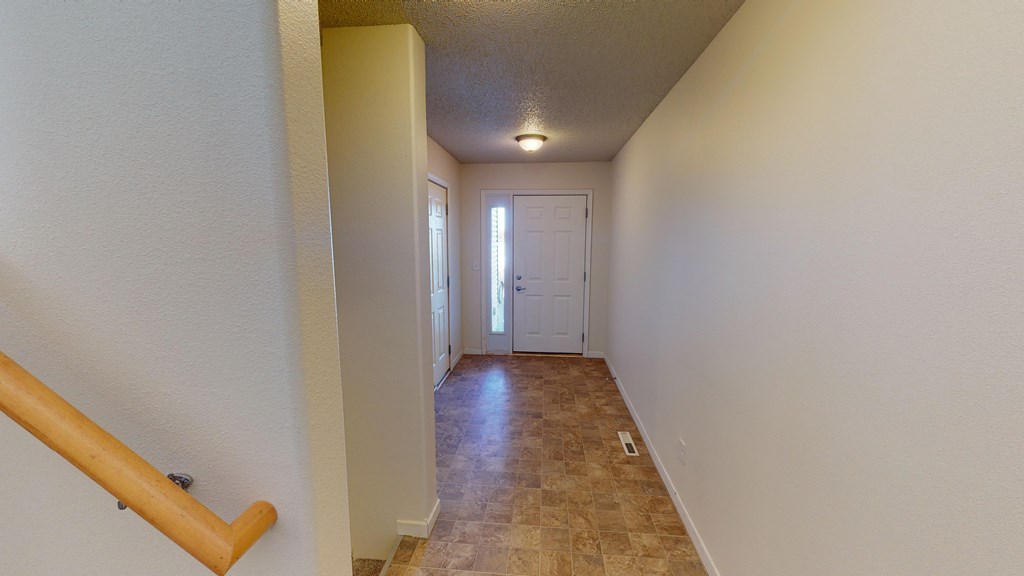 a long hallway with a white door and tiled floors and a staircase
