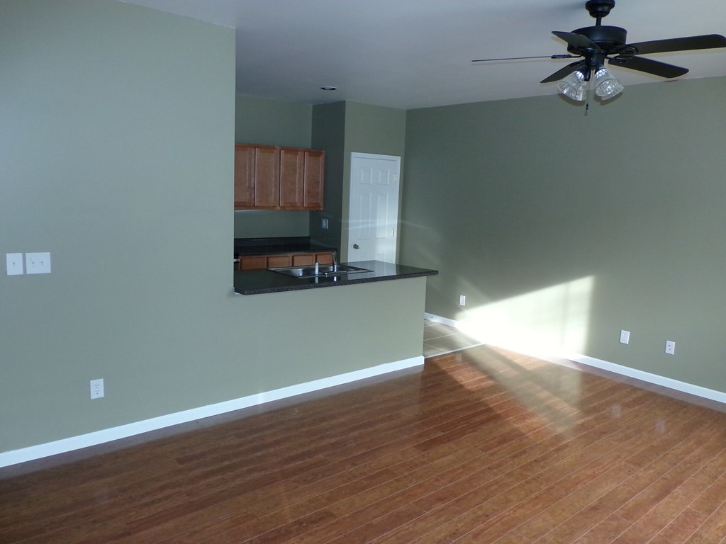 an empty living room with a kitchen and a ceiling fan
