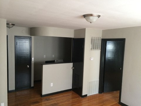 an empty living room with a kitchen and two doors