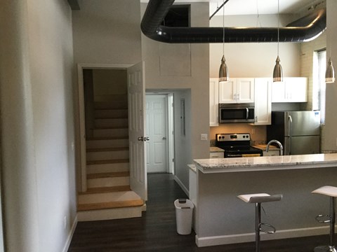 A kitchen with a white counter top and a staircase in the background.