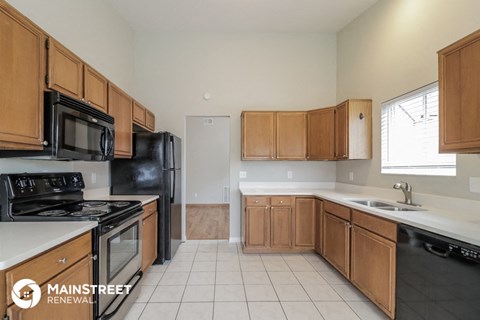 a kitchen with wooden cabinets and black appliances and white flooring