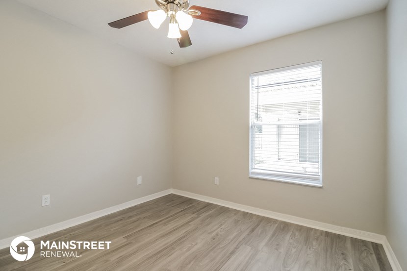 the spacious living room with wood flooring and a ceiling fan