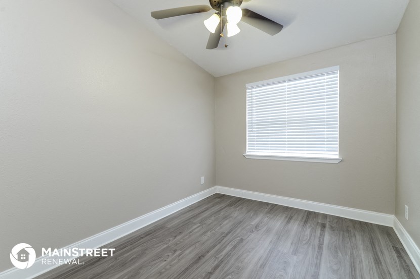 the spacious living room with wood floors and a ceiling fan