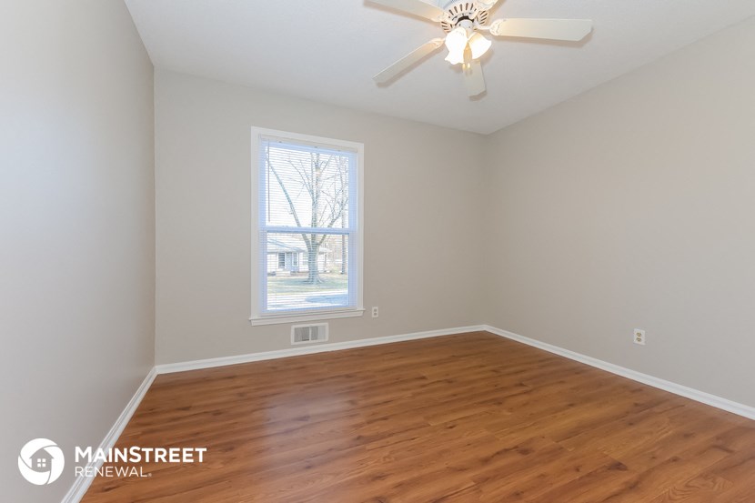 the spacious living room with wood flooring and a ceiling fan