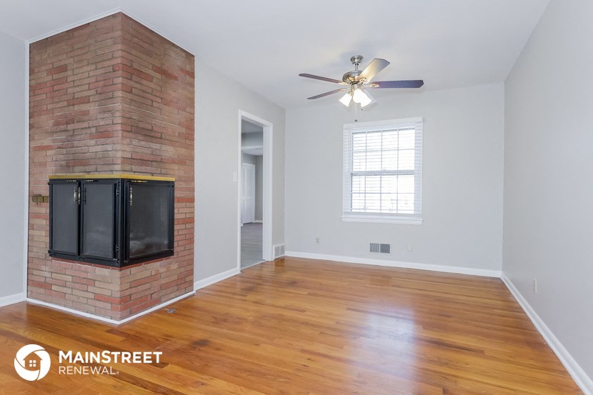the living room with wood floors and a brick fireplace and a ceiling fan