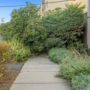 a sidewalk in a garden with bushes and trees