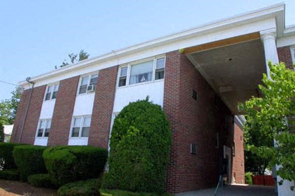 the front of a brick building with a tree and bushes