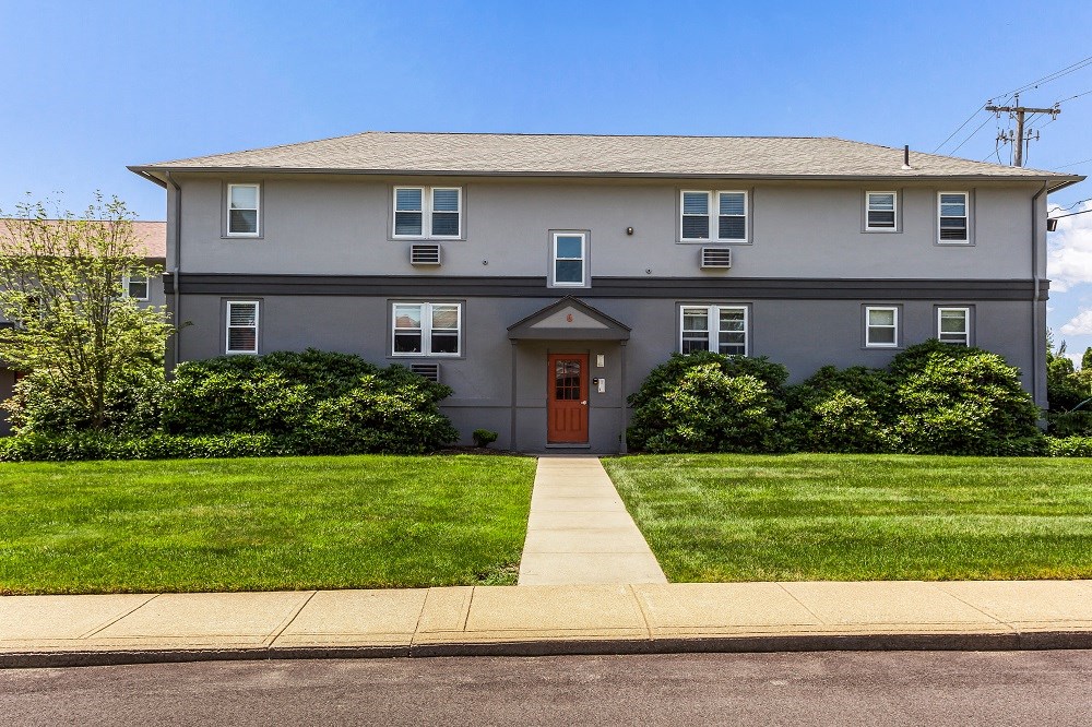 a gray house with a red door and a lawn