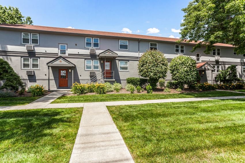 a gray apartment building with a red door and a green lawn