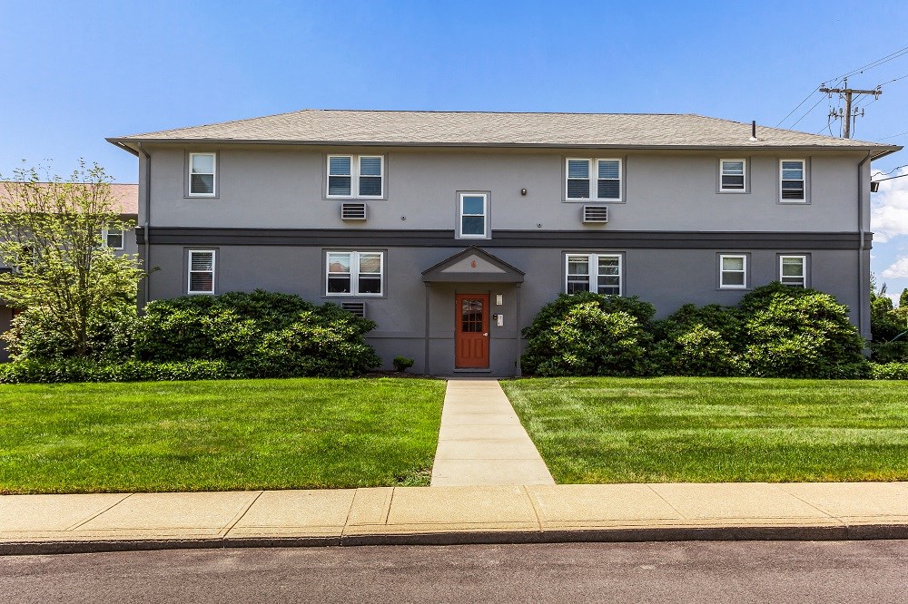 a gray house with a red door and a lawn