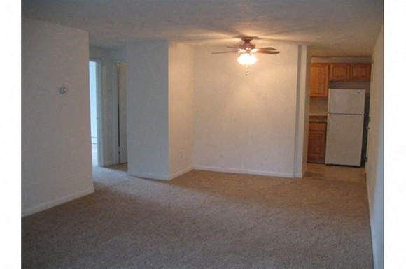 an empty living room with a ceiling fan and a refrigerator