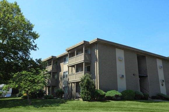 an apartment building with a green lawn and trees