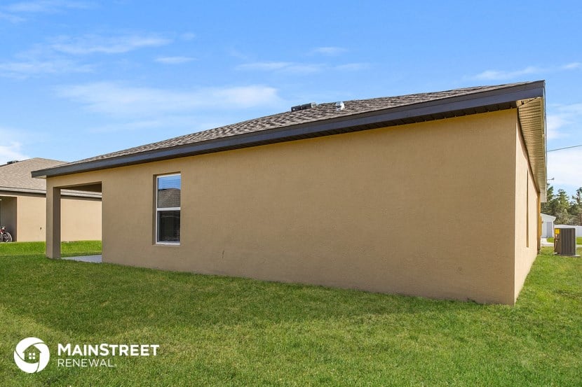 a small tan house with a roof on a grass field