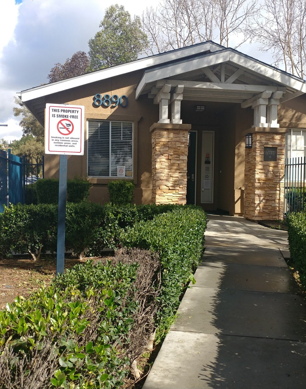 A sign is posted on a pole in front of a house stating that the property is no smoking.