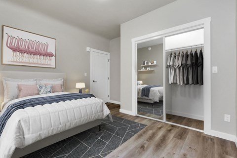 A bedroom with a large bed and a closet with clothes hanging.