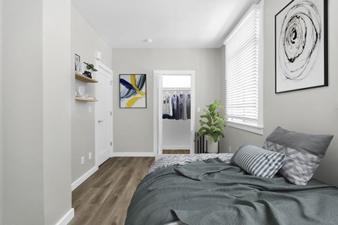 A bedroom with a bed, pillows, a plant, and a painting on the wall.