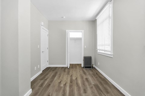 A room with a wooden floor and a window with blinds.