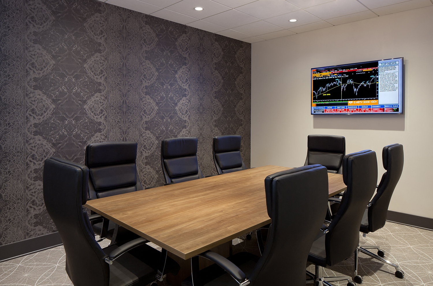 A conference room with a large table and chairs and a TV screen displaying a stock market chart.
