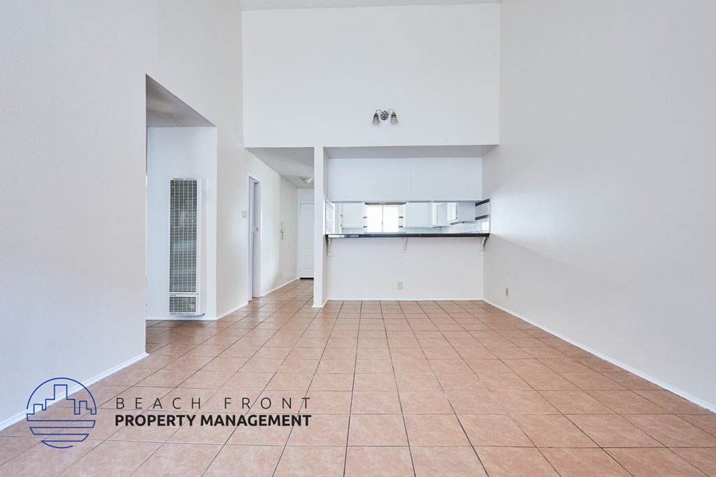 A spacious room with a tiled floor and white walls, with a logo for Beach Front Property Management in the bottom left corner.