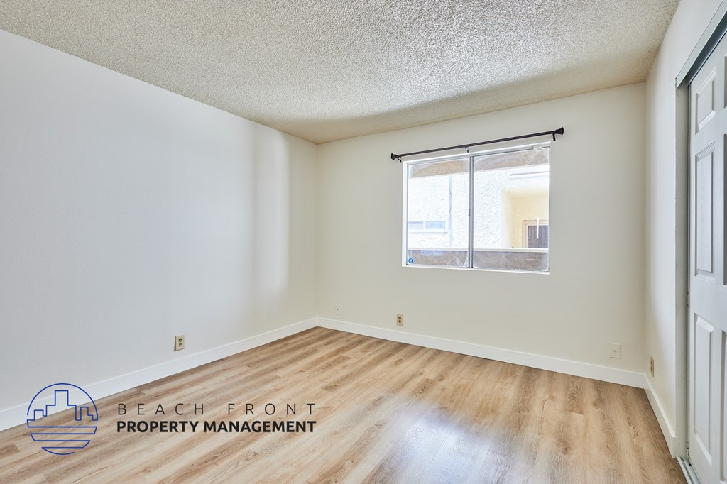 A room with a window and wooden floors is managed by Beach Front Property Management.