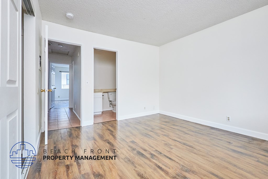 A room with wooden floors and white walls, with a logo for Beach Front Property Management in the bottom left corner.