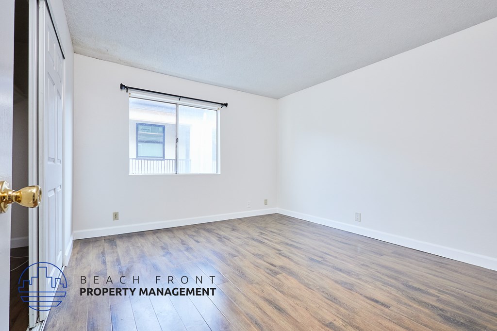 A room with wooden flooring and a window overlooking a balcony.