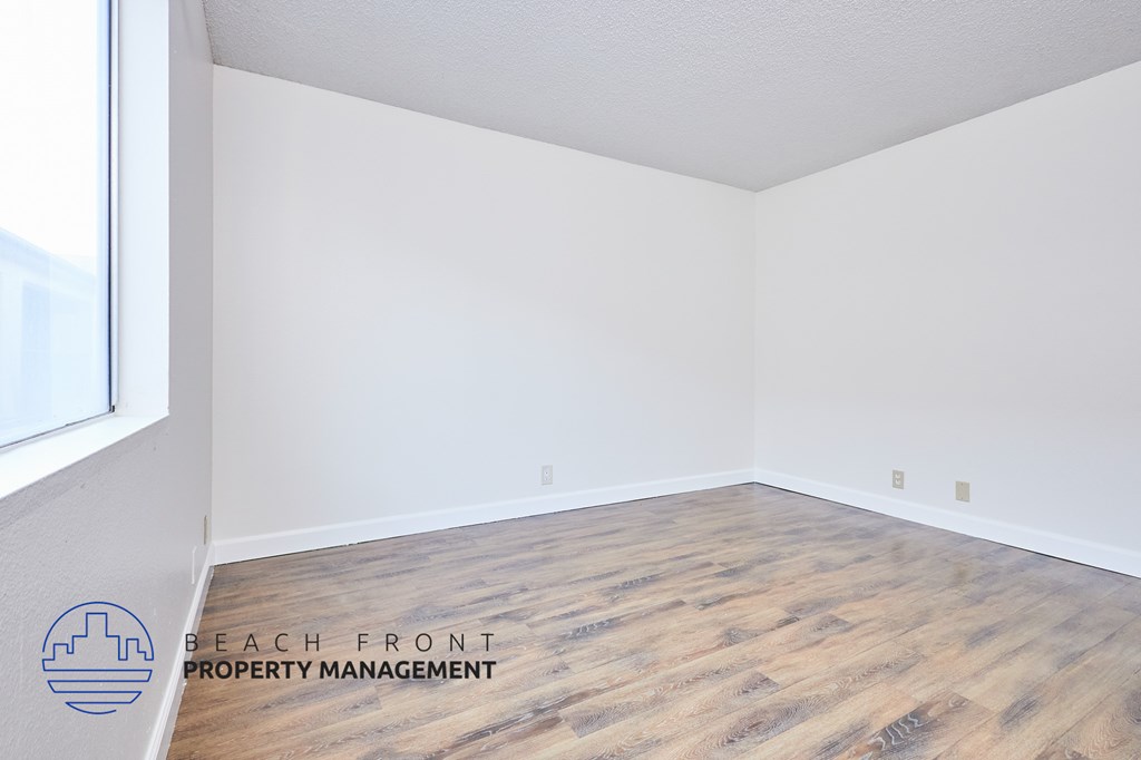 A room with wooden flooring and white walls, with a logo for Beach Front Property Management in the bottom left corner.
