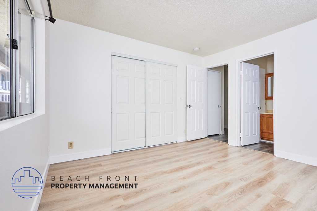 A room with white walls and wooden floors, with a logo for Beach Front Property Management in the bottom left corner.