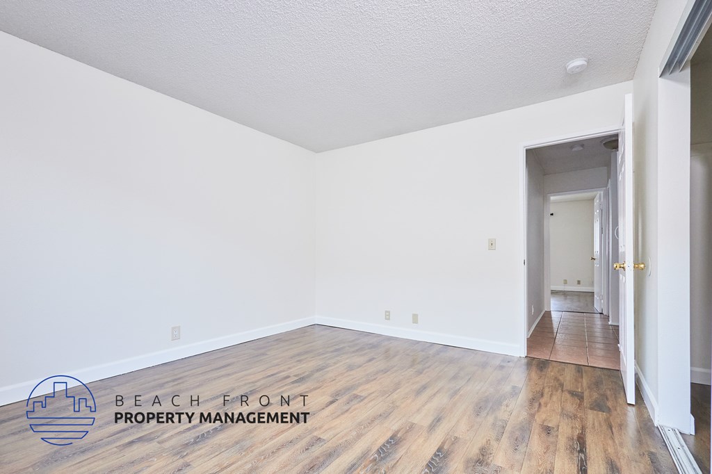A room with wooden floors and white walls, with a doorway leading to another room.