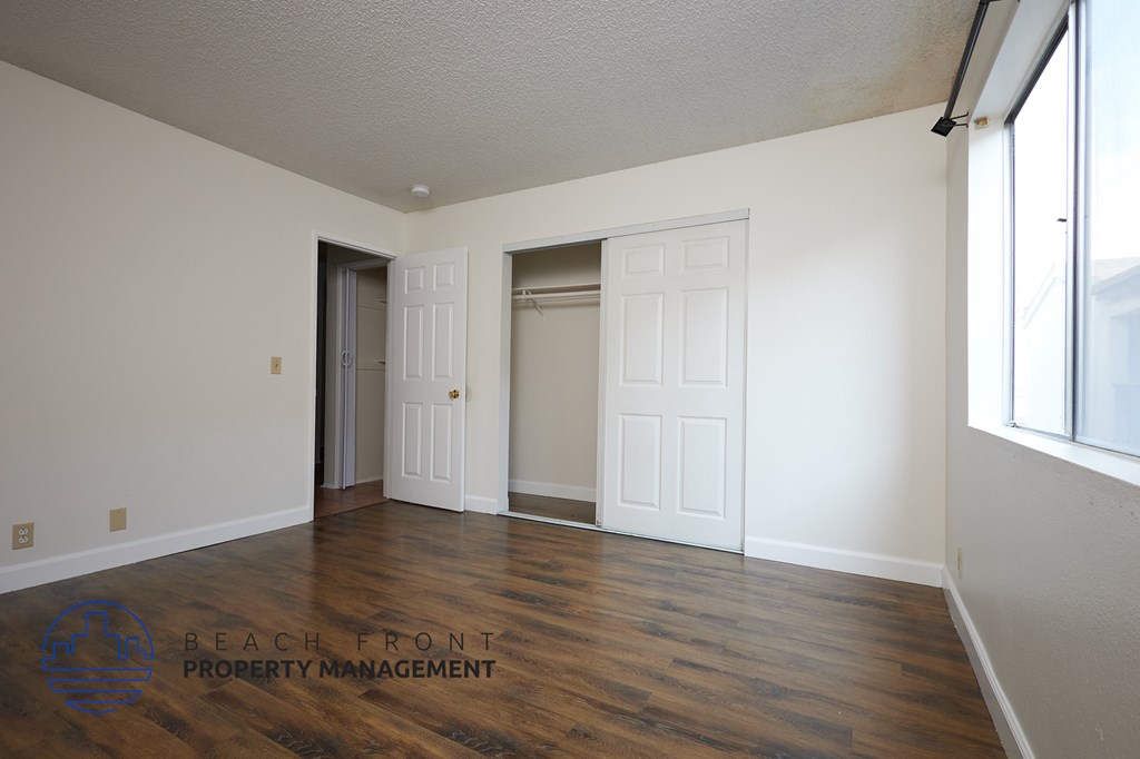 A room with wooden floors and white walls, with a logo for Beach Front Property Management in the bottom left corner.