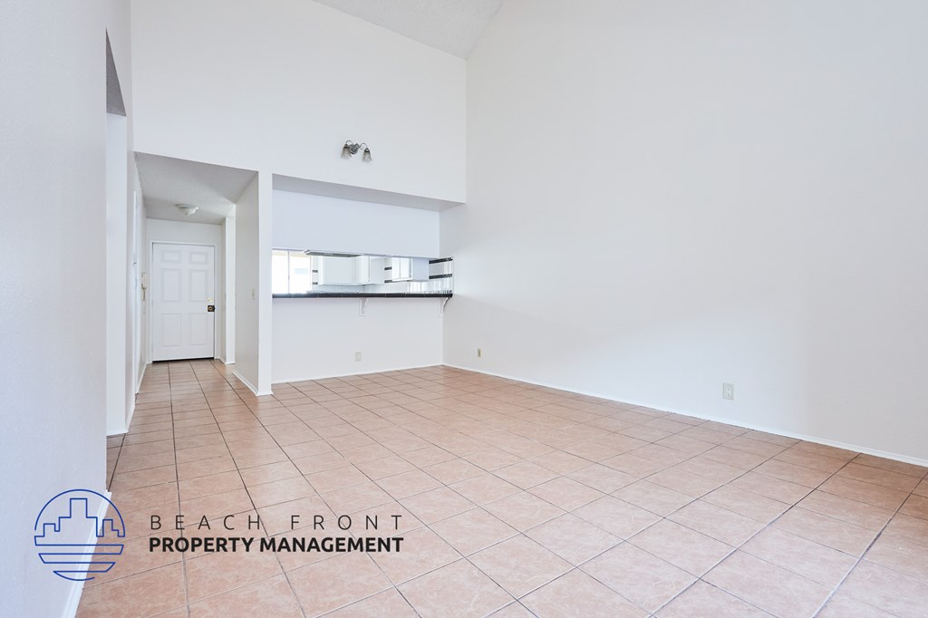 A spacious room with tiled flooring and a logo for Beach Front Property Management in the corner.