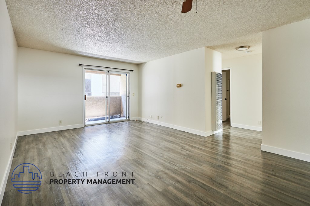 A spacious room with wooden flooring and a sliding glass door leading to a balcony.