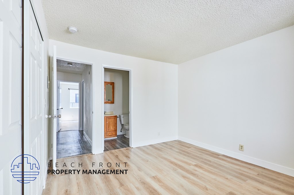 A room with a wooden floor and white walls, with a doorway leading to another room.